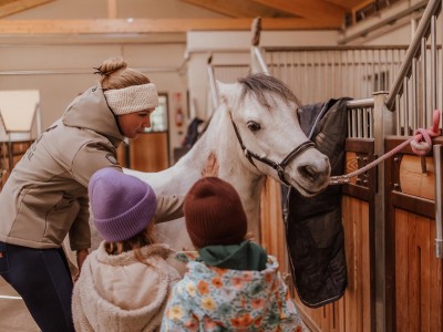 Un'istruttrice di equitazione e due bambini sono in piedi accanto a un giovane cavallo, legato alla stalla.