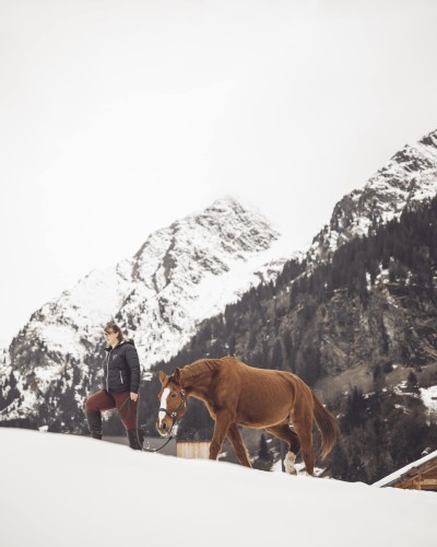 Istruttrice di equitazione passeggia con il cavallo nella neve