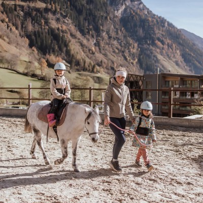 Reitlehrerin begleitet ein Kind, was wiederrum ein Pony mit einem Kind begleitet