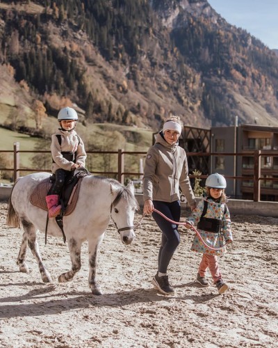 Reitlehrerin begleitet ein Kind, was wiederrum ein Pony mit einem Kind begleitet