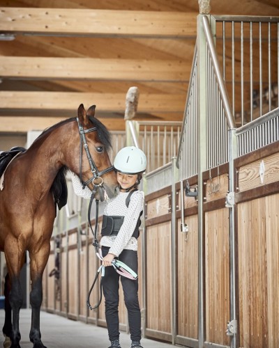 Bambino piccolo in piedi accanto a un cavallo in un maneggio
