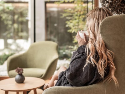 Una donna è seduta su una poltrona e beve una bevanda calda.