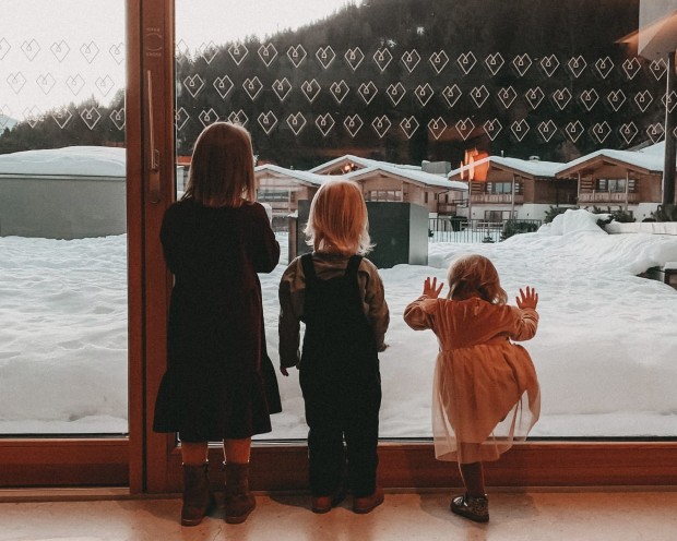 3 bambini sono in piedi davanti alla finestra e guardano fuori.