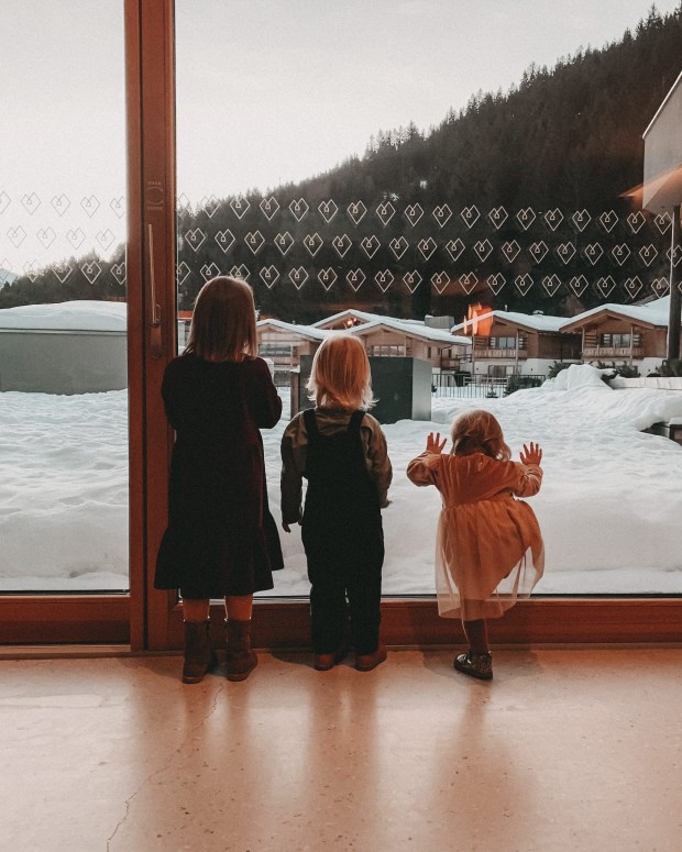 3 Kinder stehen bei einer Fensterscheibe und schauen nach außen