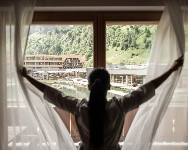 Cameriera che apre le tende in una camera con vista sul resort Feuerstein.