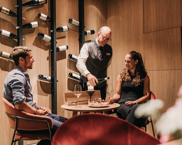 Degustazione di vini con due ospiti al bar del Feuerstein con bottiglie a parete.