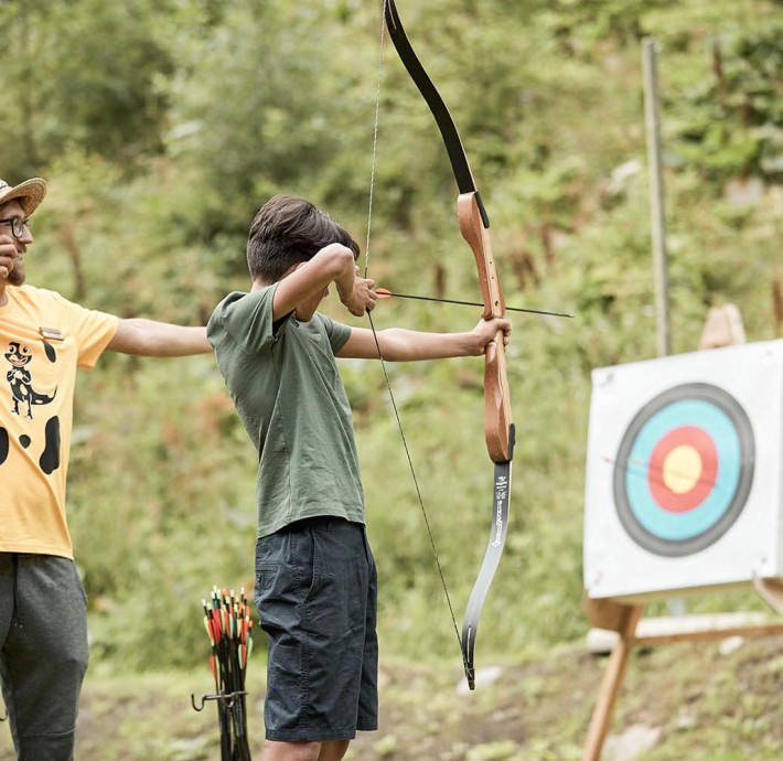 Supervisor shows a teenager how to shoot a bow