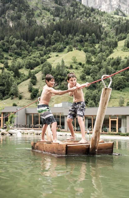 Two boys pull themselves in the pond on a raft to the end of the pond