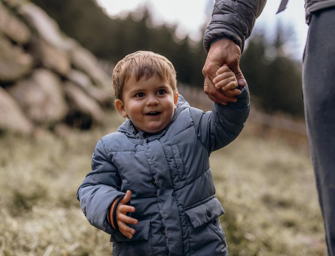 Kleines Kind geht Hand-in-Hand mit Elternteil spazieren