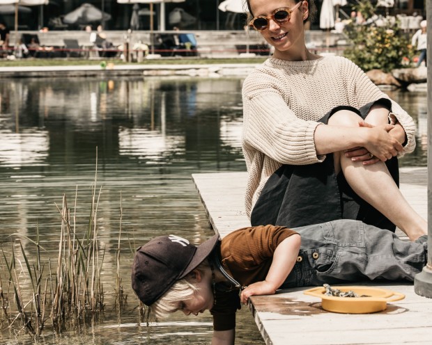 Kleines Kind liegt auf dem Bauch und streckt den Arm in den Teich