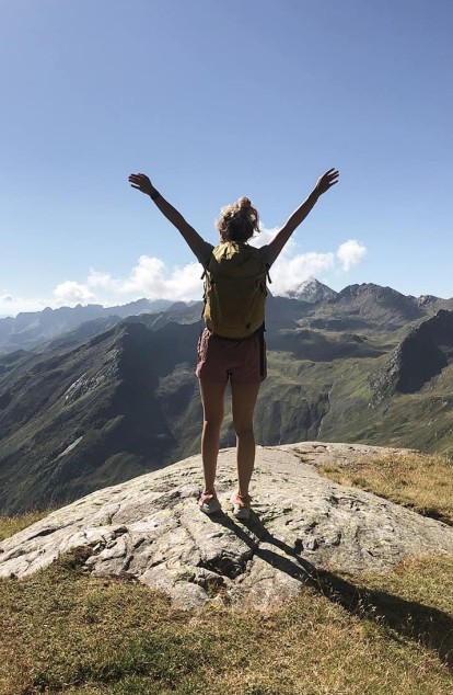 Una donna in cima a una montagna alza le braccia verso il cielo