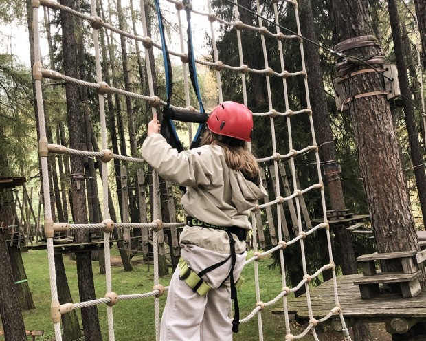 Un adolescente con casco e imbracatura scala una rete di corda nel parco avventura
