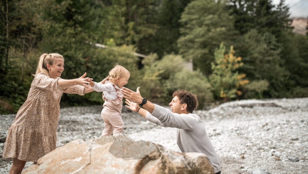 Una bambina piccola cammina su una pietra e i genitori la tengono stretta