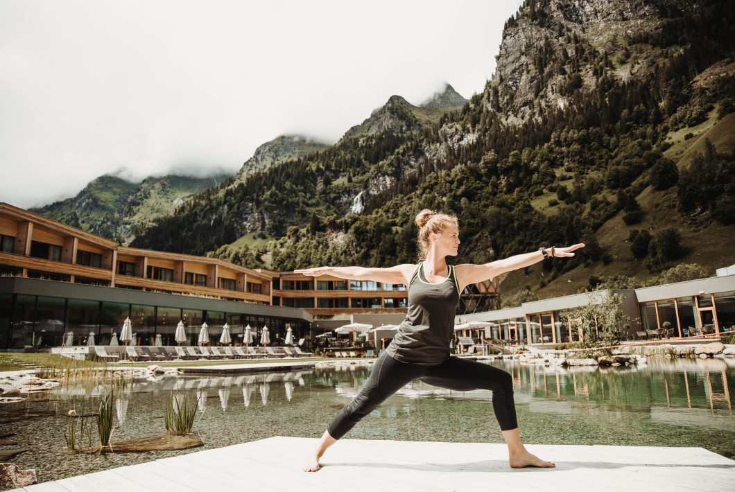 Una donna pratica una posizione yoga all'aperto con vista sulle montagne e sull'hotel