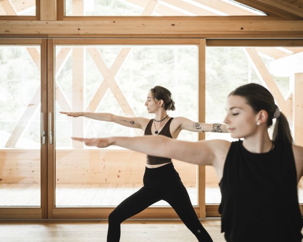 Due donne fanno yoga in piedi in una sala luminosa con vista sulle montagne