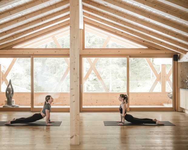 Due donne fanno esercizi di stretching in una sala yoga con travi in legno