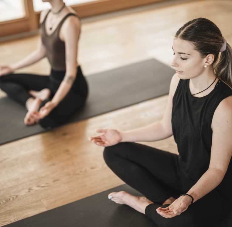 Due donne meditano sedute su tappetini in una sala yoga