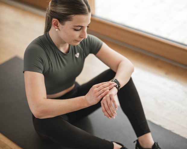 Donna seduta su un tappetino da yoga guarda il suo orologio sportivo