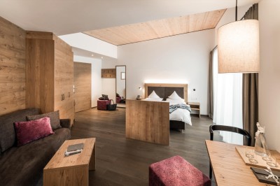 A spacious hotel room with wooden interiors, a cozy seating area, and a large bed.