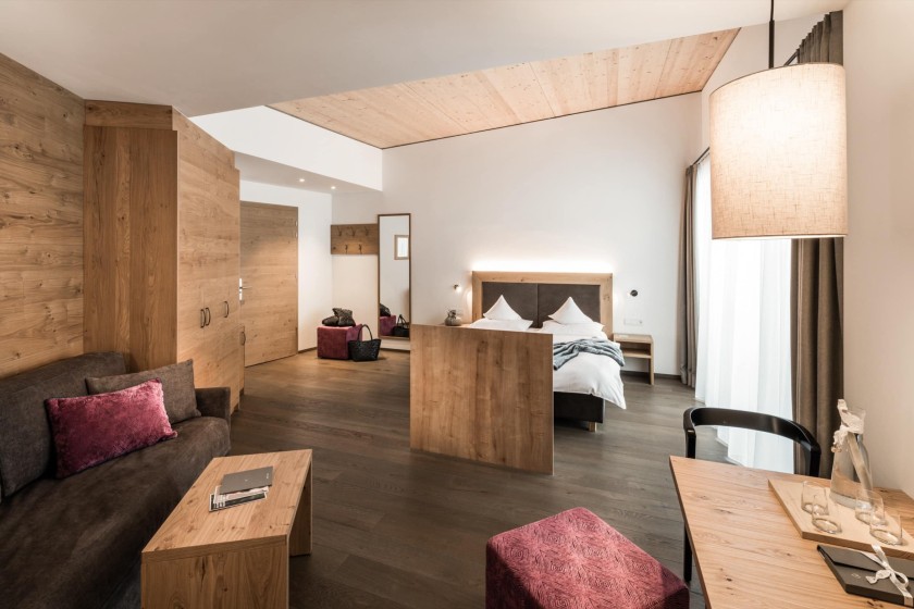 A spacious hotel room with wooden interiors, a cozy seating area, and a large bed.