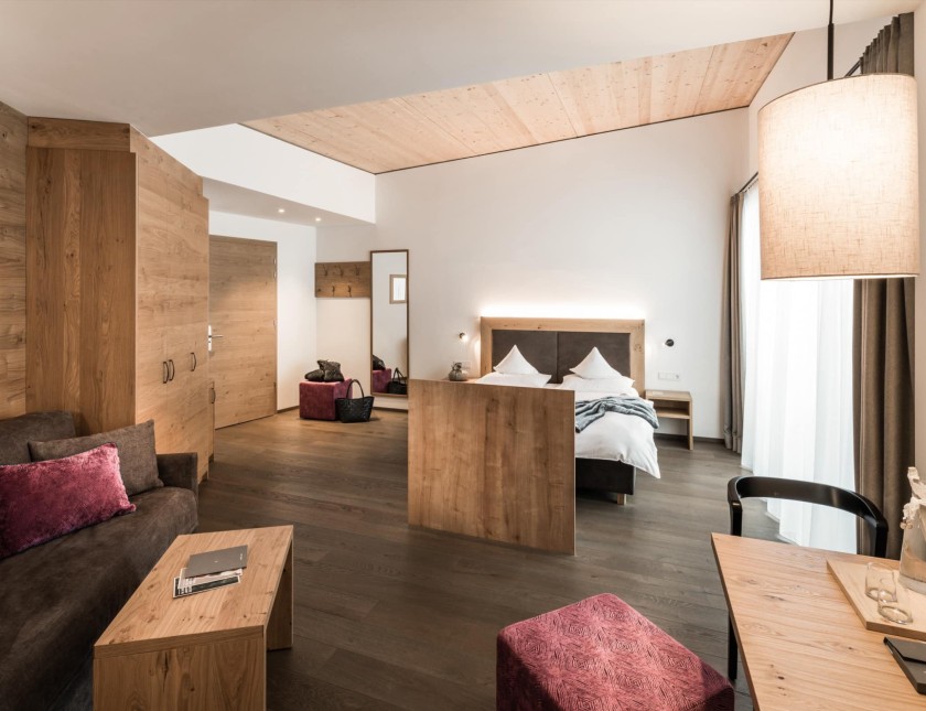 Una spaziosa camera d'hotel con interni in legno, un'accogliente area salotto e un grande letto.