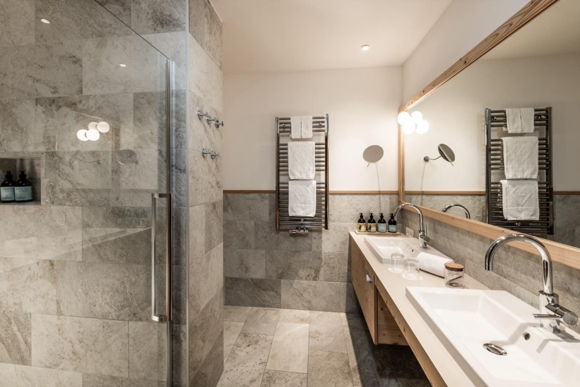 Un bagno luminoso e moderno con un grande lavandino, specchio e doccia a filo pavimento.