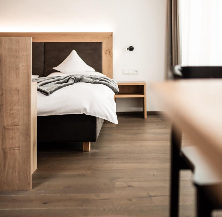 Un accogliente letto d'hotel con illuminazione calda e decorazioni in legno in stile alpino moderno.